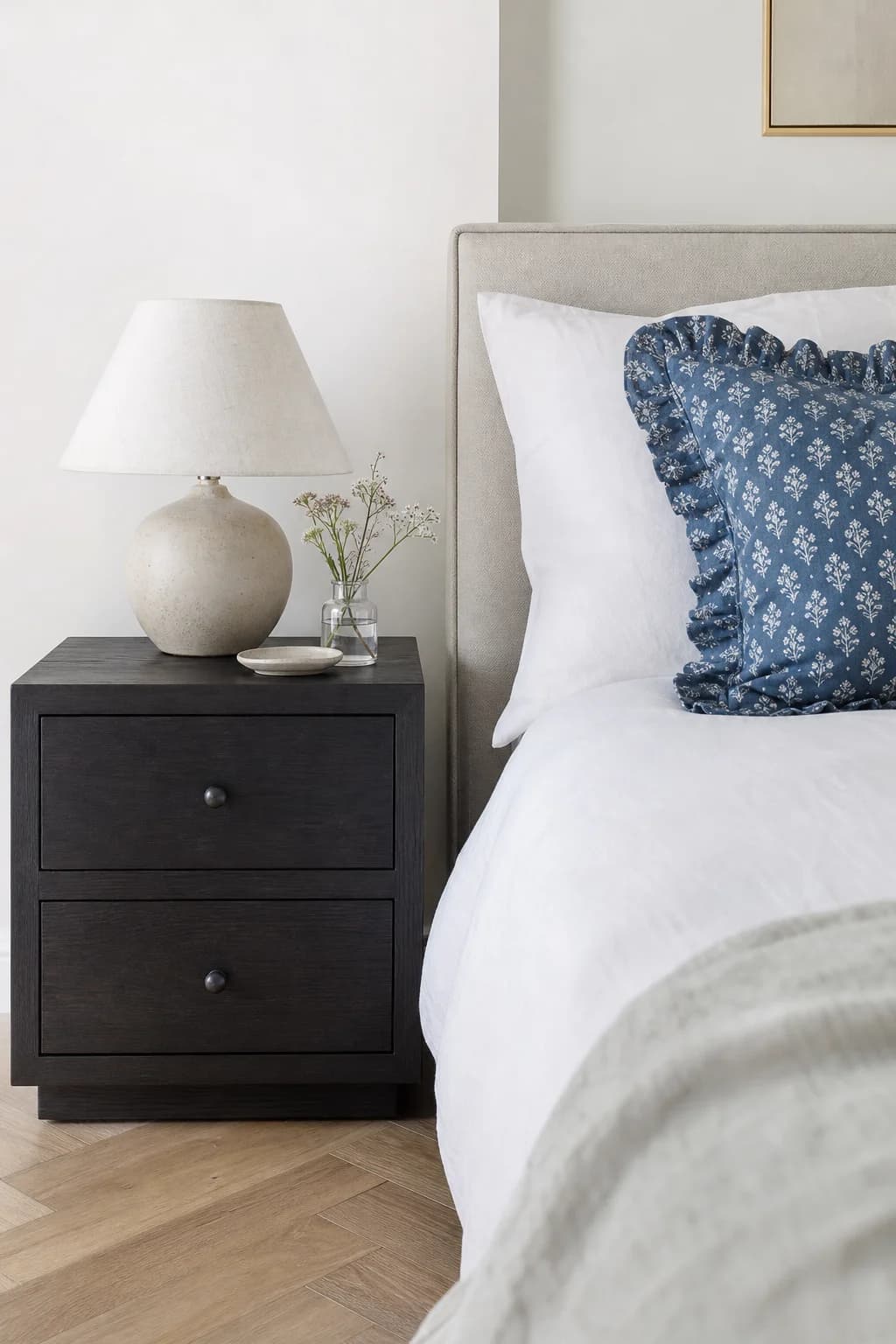 Ebony bedside table beside a bed with a blue velvet cushion